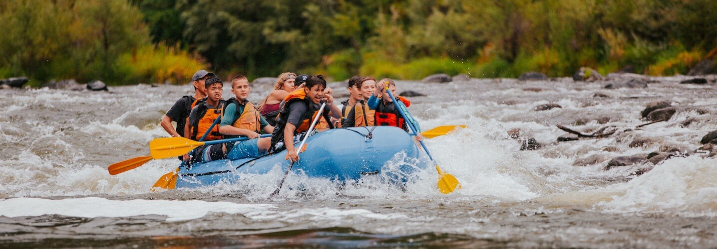 Group of people white water rafting on a river with rapids.