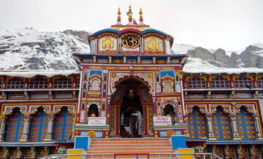 A colorful Hindu temple with intricate architecture set against snow-covered mountains and a clear sky.