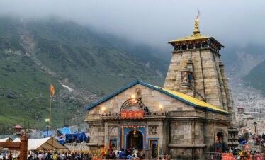 Kedarnath Temple surrounded by misty mountains with devotees gathered near the shrine.