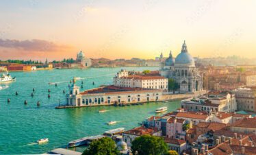 An elevated view of Venice at sunset, featuring the Grand Canal and the iconic dome of the Santa Maria della Salute basilica.