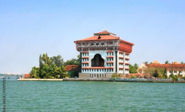 A historic waterfront building with traditional architecture surrounded by water and palm trees under a clear blue sky.