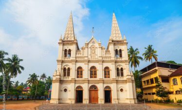 A grand white church with twin spires, palm trees, and a clear blue sky in the background.