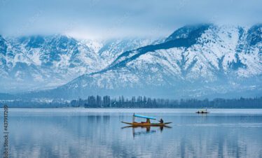 A lone shikara boat glides across the calm, reflective surface of Dal Lake against a backdrop of towering, snow-dusted mountains.