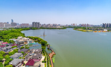 An aerial view of a city skyline surrounding a large lake with residential houses and greenery along the shoreline under a clear sky.