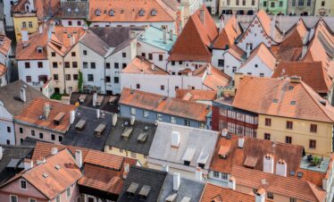 An aerial view of a European town showcases a dense cluster of historic buildings with charming red and grey tiled roofs and white chimneys.