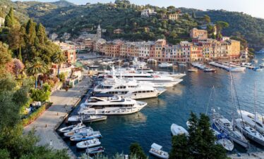 A high-angle view of Portofino's colorful harbor filled with luxury yachts and boats against a backdrop of lush green hills and Italian architecture.