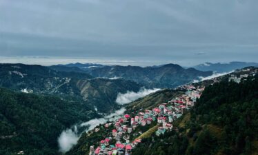 A panoramic view of a hill town with colorful houses along mountain ridges surrounded by mist and lush green valleys.